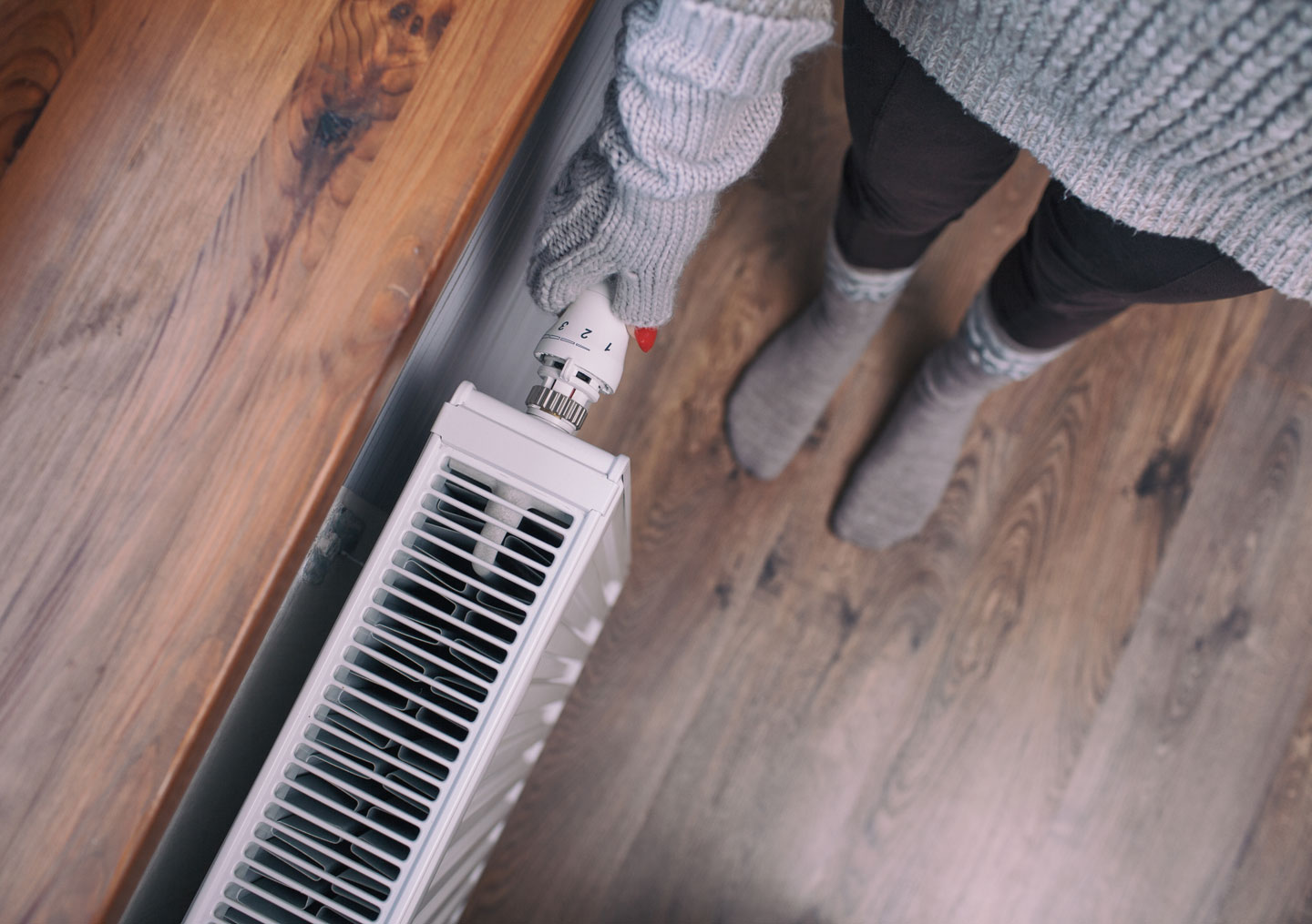 Close,Up,Of,Woman,Hands,Wearing,Woolen,Gloves,Turning,Heater